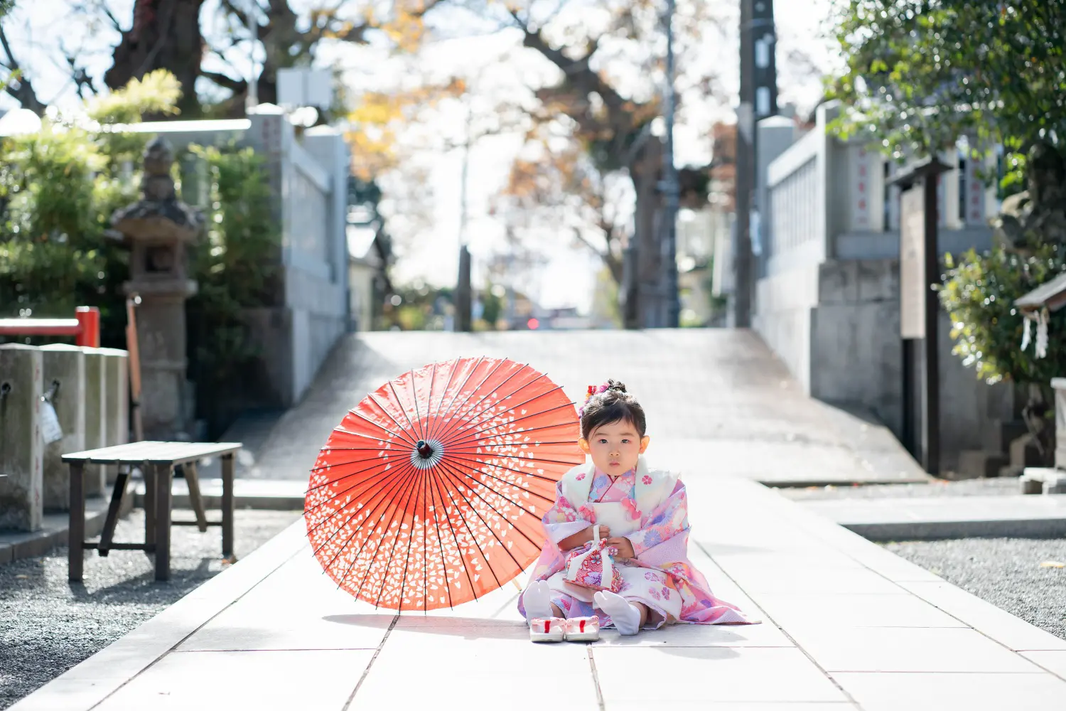 六所神社の参道の中央に座る被布姿の3歳の女の子と赤い和傘（大磯・七五三出張撮影）