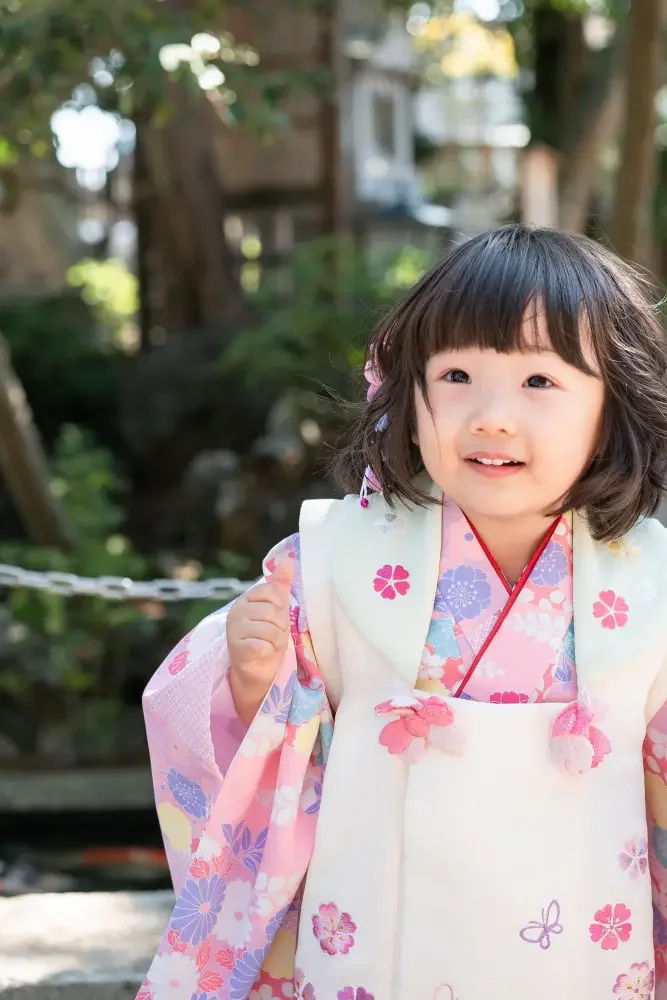 池のほとりで大きく笑う、クリーム色の被布姿の3歳の女の子の七五三出張撮影（六所神社）