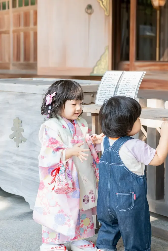 六所神社の奉納箱の脇で弟と向き合って笑う、被布姿の3歳の女の子の七五三出張撮影