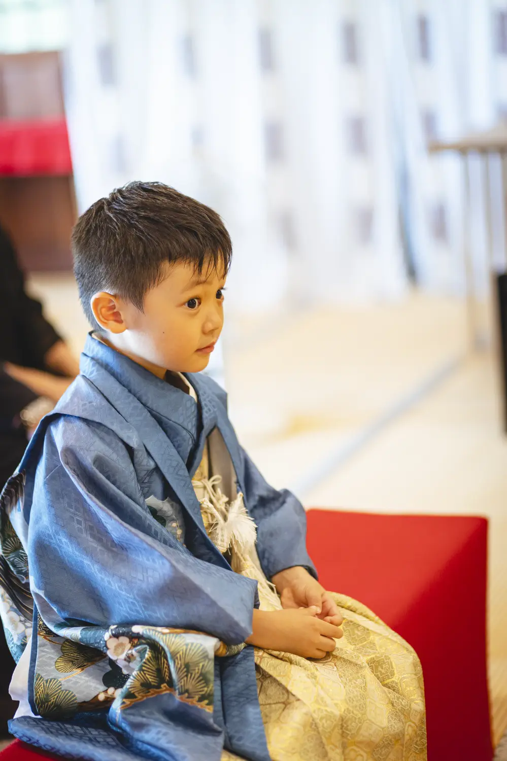 社殿内の赤い座椅子に腰かけてご祈祷を待つ5歳の男の子の横顔、青い羽織袴（七五三・六所神社）