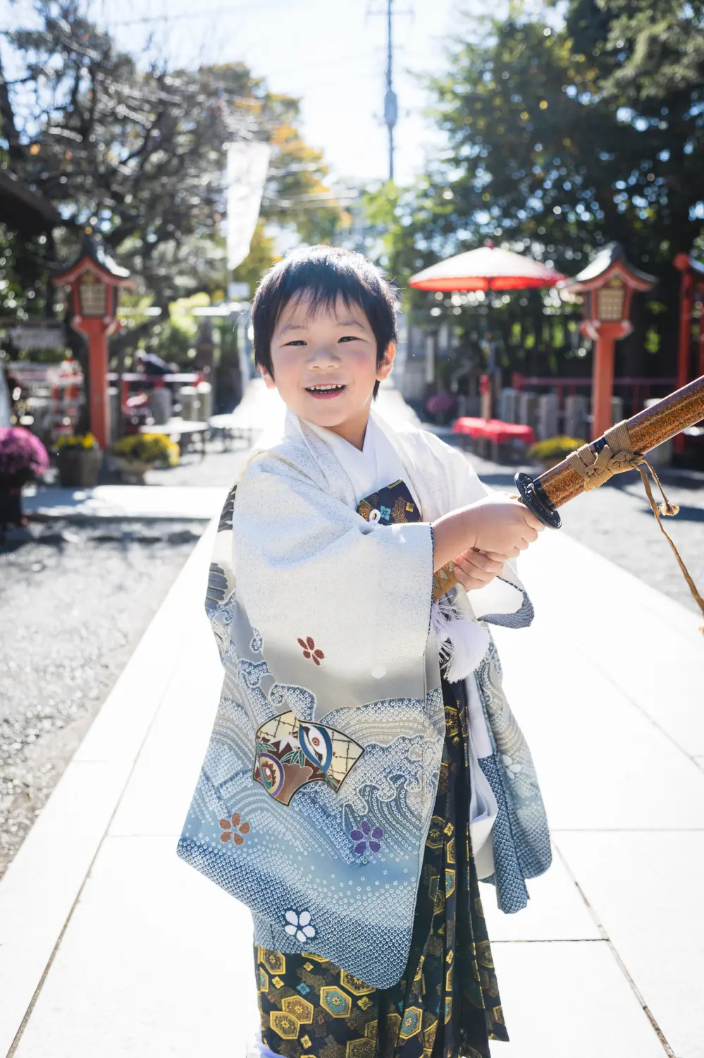 朱塗りの灯籠と赤傘を背に白い石畳の参道で笑う5歳の男の子、生成りの羽織袴の七五三撮影（六所神社・大磯）