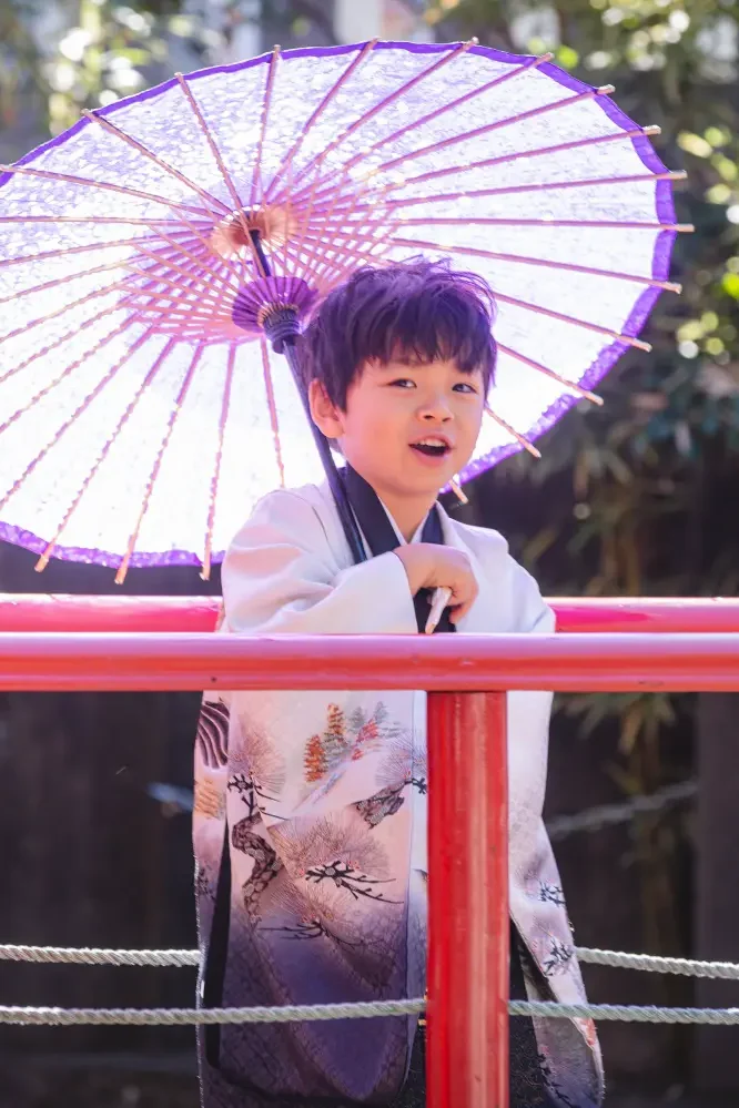 朱塗りの柵越しに紫の和傘を差して話す5歳の男の子、七五三出張撮影（六所神社・大磯）
