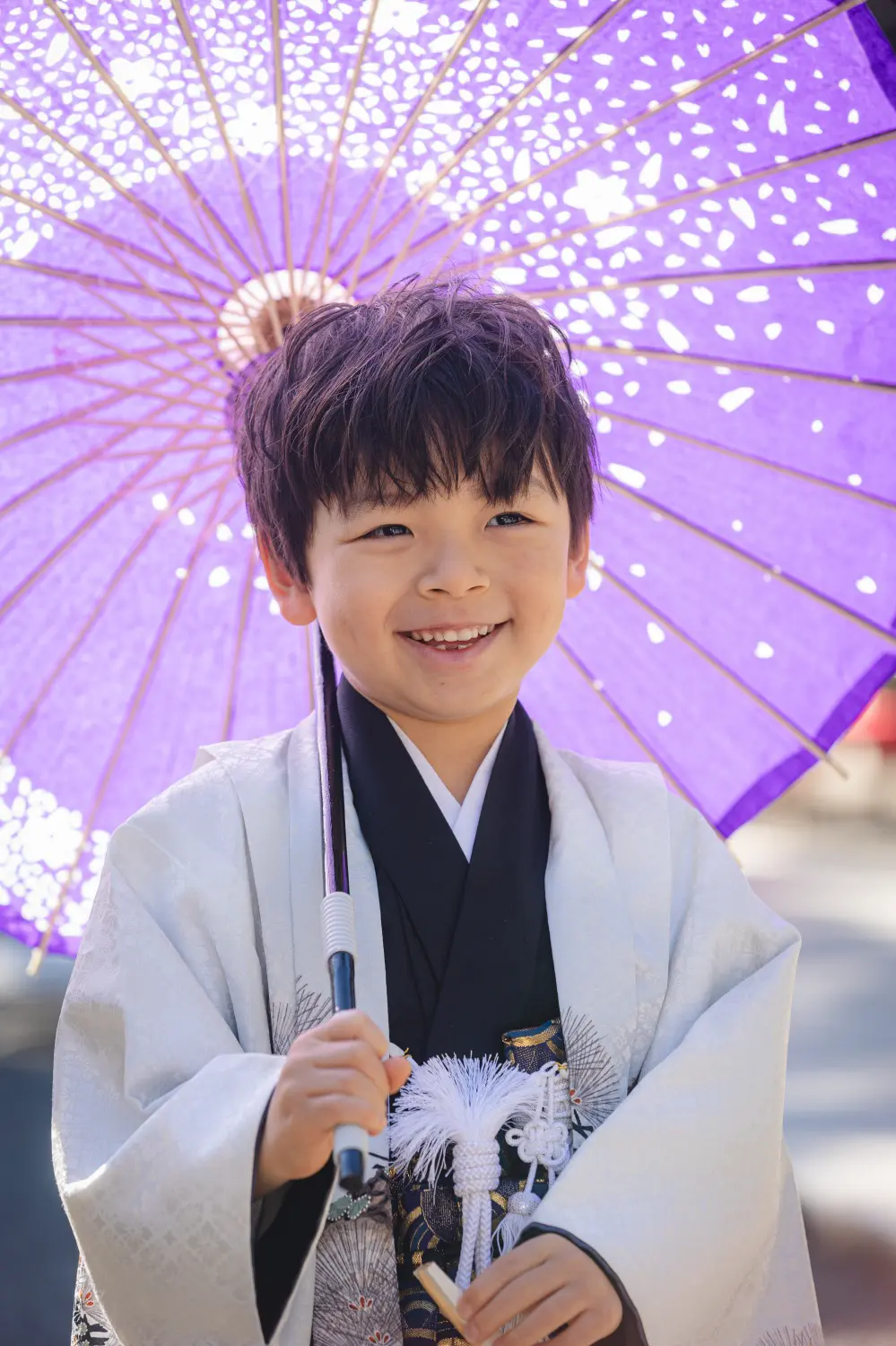 紫の和傘を差して満面の笑みを見せる5歳の男の子、白い羽織姿の七五三（六所神社・大磯）