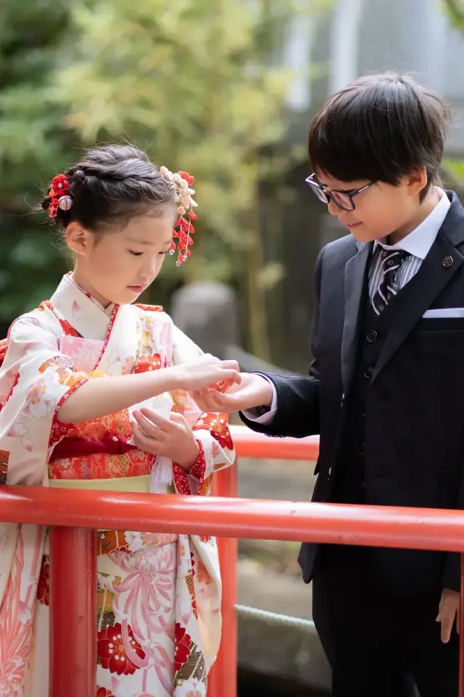 太鼓橋の上で兄から手のひらに紙を受け取る7歳の女の子、七五三の兄妹（六所神社・大磯）