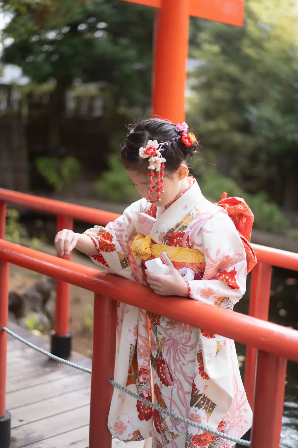 朱の欄干から池をのぞき込む7歳の女の子の後ろ姿、四つ身と下がり飾り（六所神社・七五三）