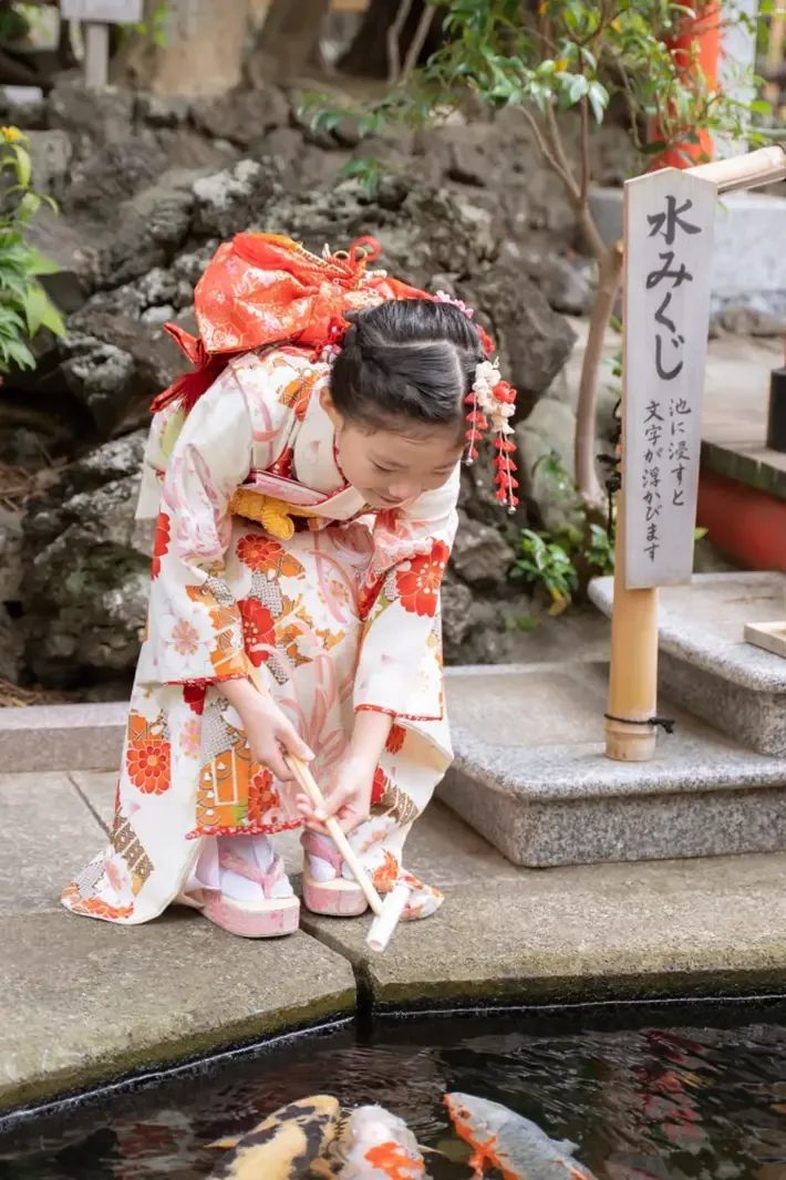 「水みくじ」の立札の脇でおみくじを池に浸す7歳の女の子、六所神社の七五三（神奈川県大磯町）