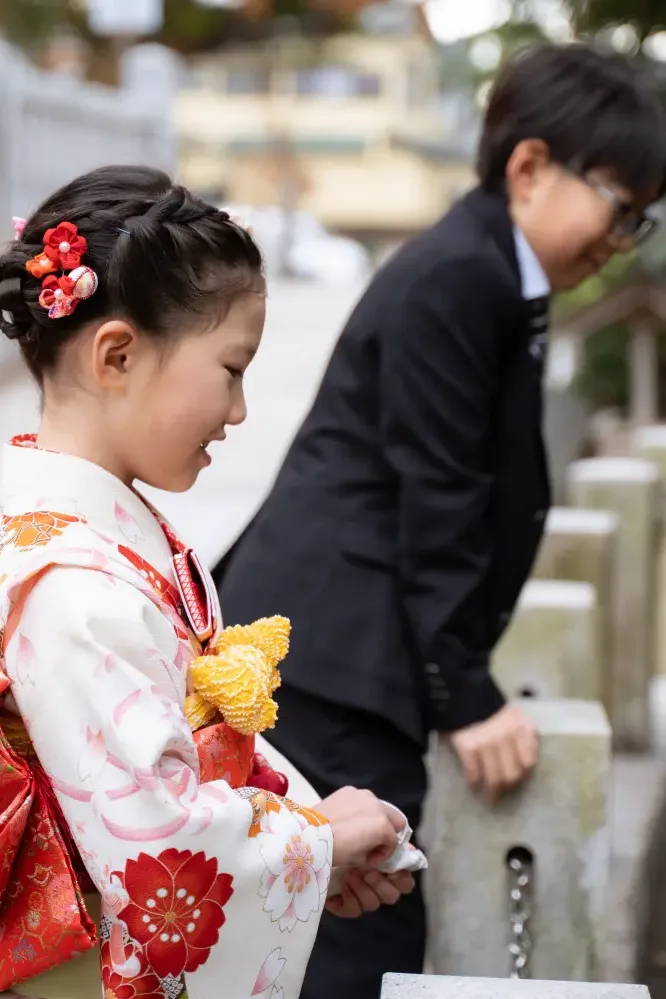 参道で小さく折った紙を手にする7歳の女の子と黒いスーツの兄、七五三（六所神社・大磯）