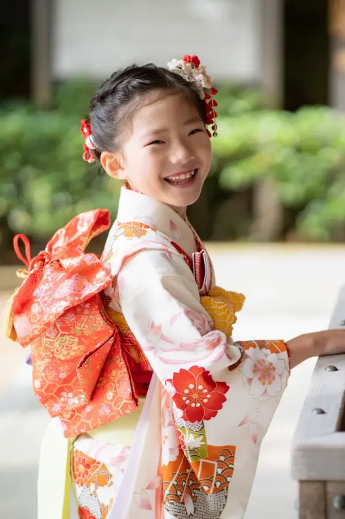六所神社の手水舎で木の水盤に手をのせて笑う7歳の女の子、四つ身姿の七五三（神奈川県大磯町）
