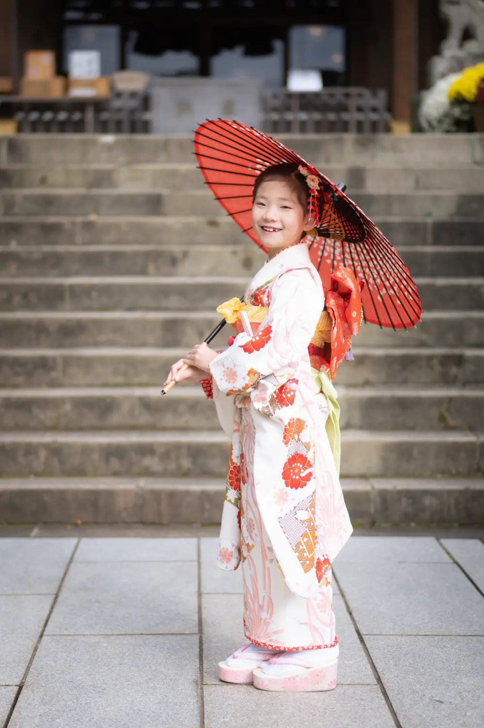 朱の和傘を差して石段の前に立つ7歳の女の子の全身、四つ身姿の七五三（六所神社・大磯）