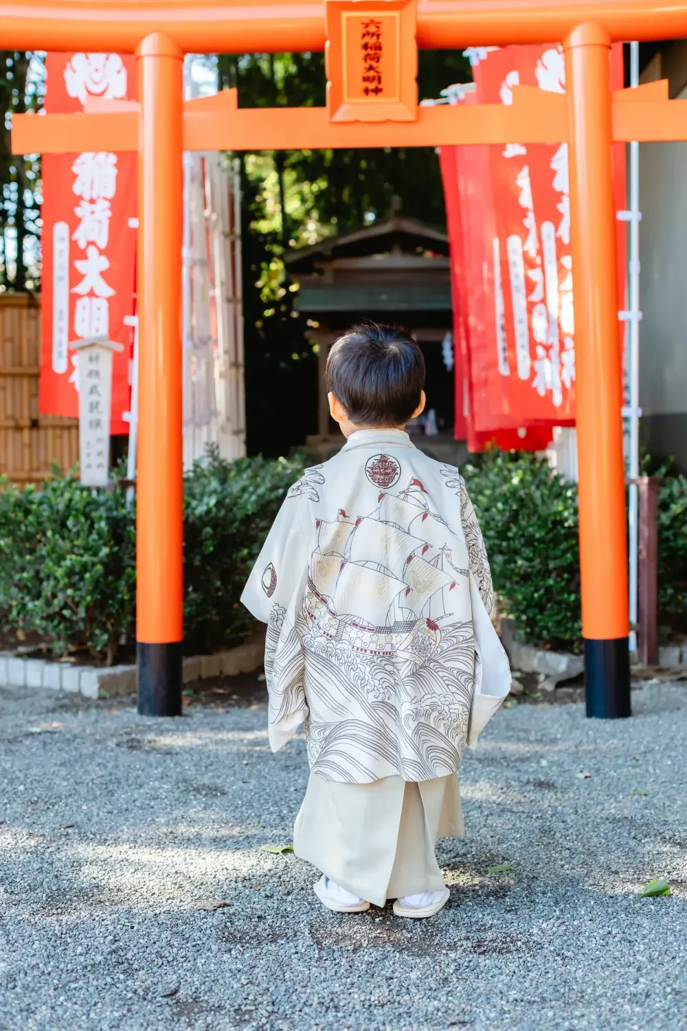 鳥居に向かって立つ男の子の後ろ姿、生成りの羽織の背に宝船と波を線描きした七五三の衣装（六所神社・大磯）