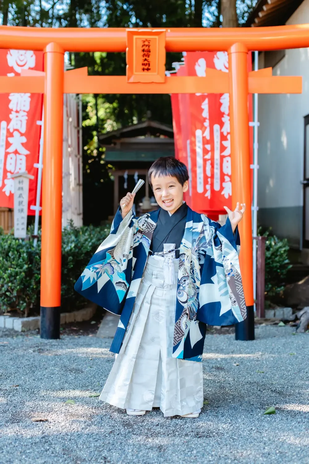 両手を高く上げてはしゃぐ濃紺の羽織袴の男の子、朱い鳥居とのぼり旗を背にした七五三出張撮影（六所神社・大磯）