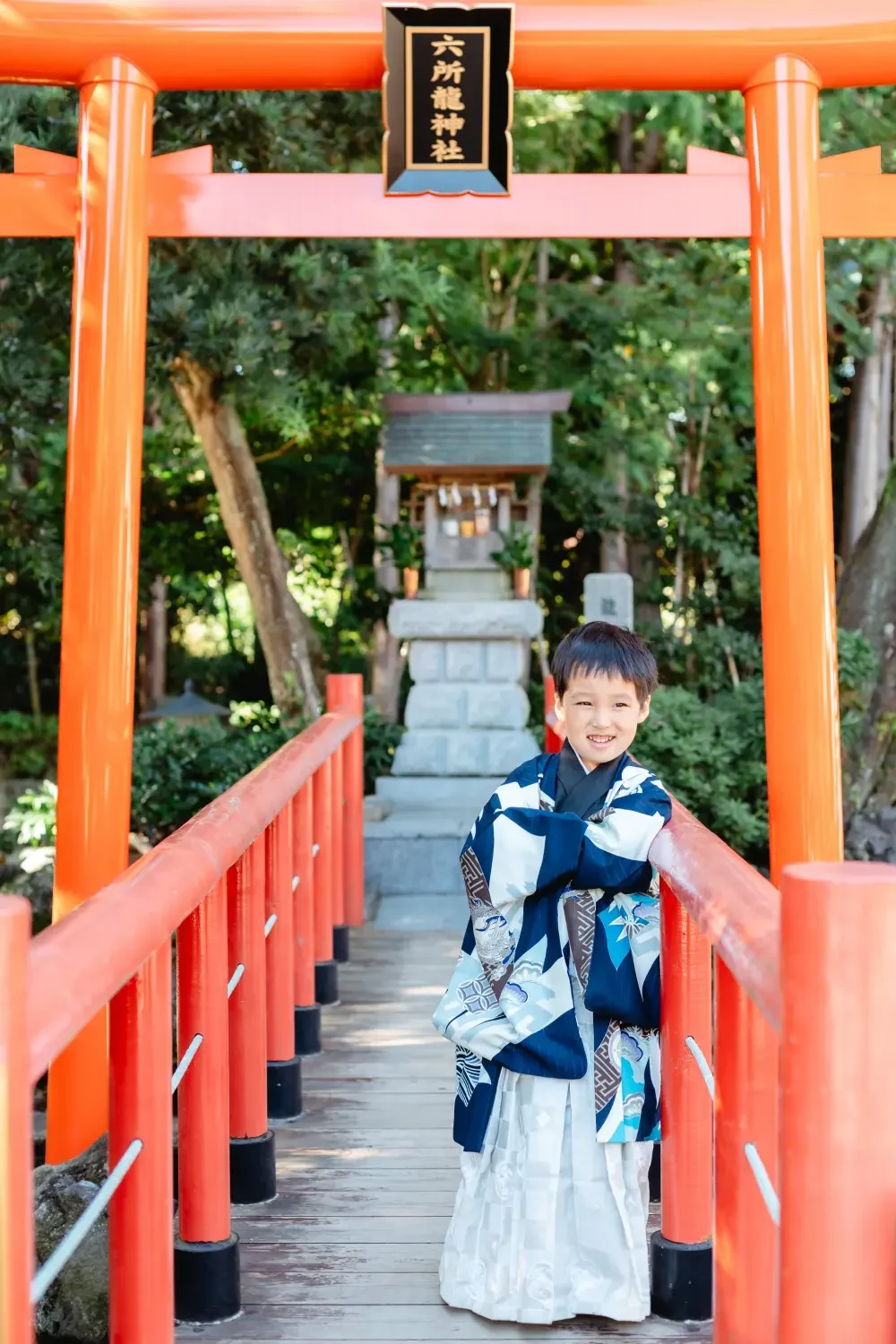 朱塗りの太鼓橋の欄干に寄りかかって笑う、濃紺の羽織袴の男の子の七五三出張撮影（六所神社・大磯）