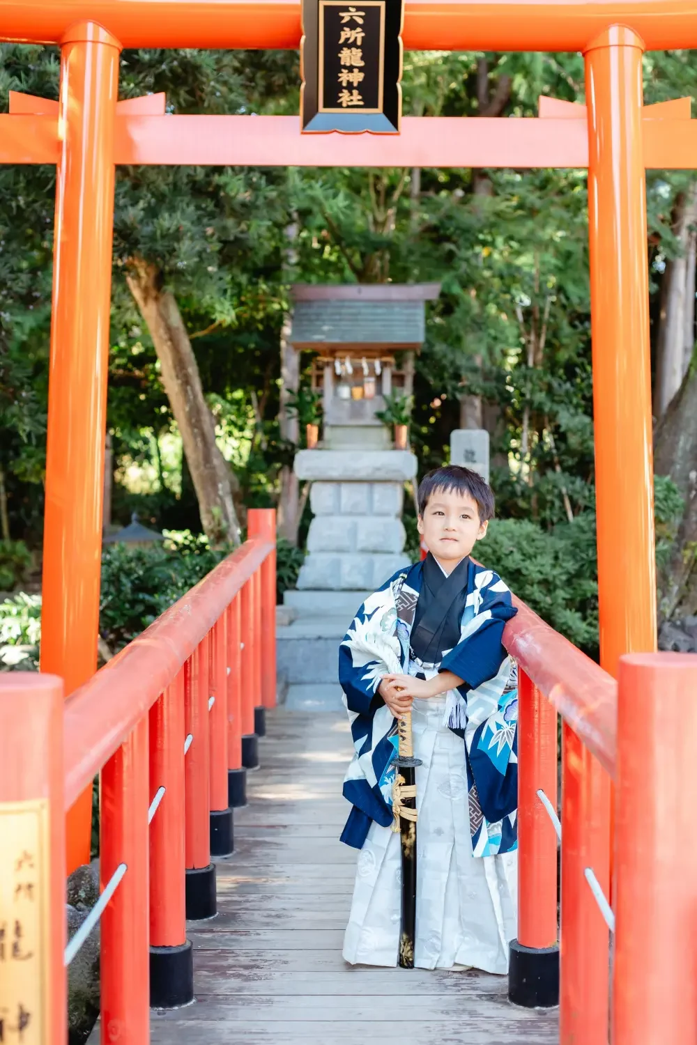 「六所龍神社」の扁額がかかる朱い鳥居と太鼓橋の上に立つ、濃紺の羽織袴の男の子の七五三出張撮影（六所神社・大磯）