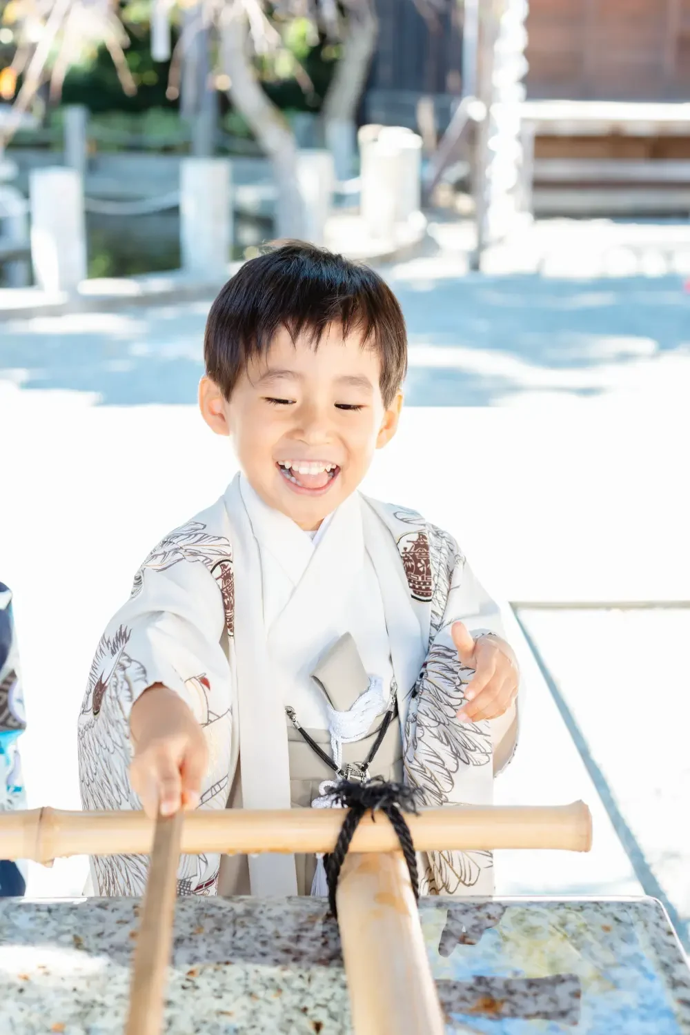 手水舎の柄杓に手を伸ばして笑う、生成りの羽織袴の男の子の寄り、七五三出張撮影（六所神社・大磯）