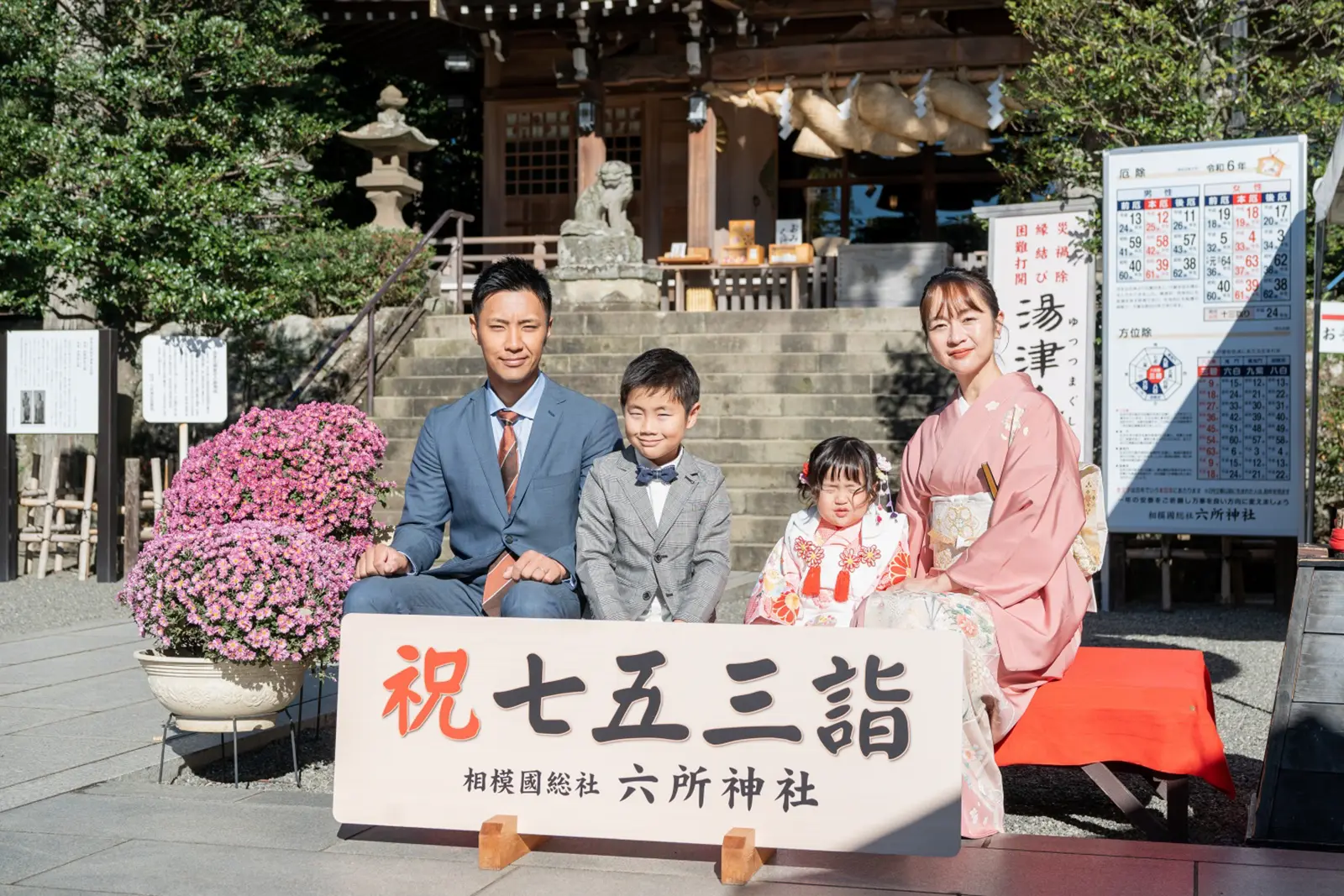 祝七五三詣 相模國総社 六所神社の看板の後ろに座る家族4人、被布姿の3歳の女の子（大磯）