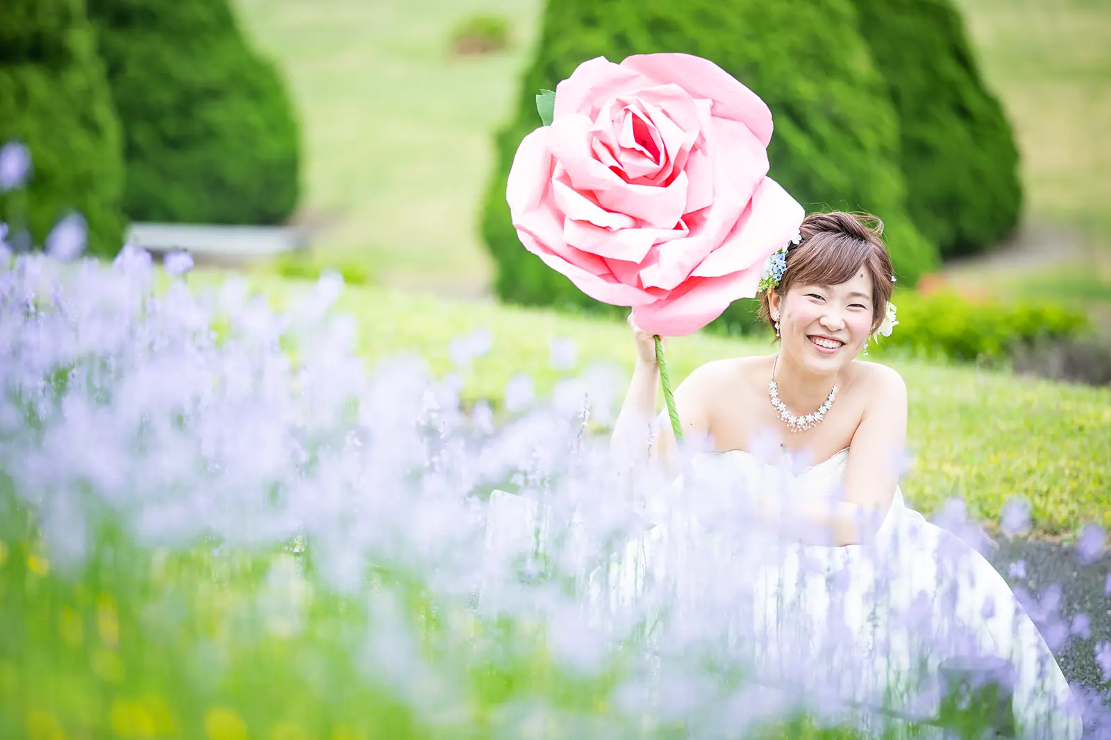 大きなピンクのバラを持って笑う新婦を写したフォトウェディング写真
