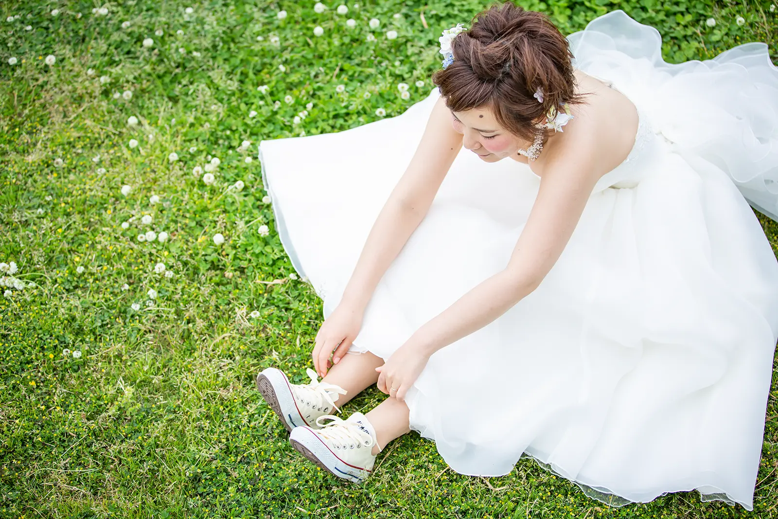 芝生の上で座りながらスニーカーの靴ひもを結ぶ新婦の写真