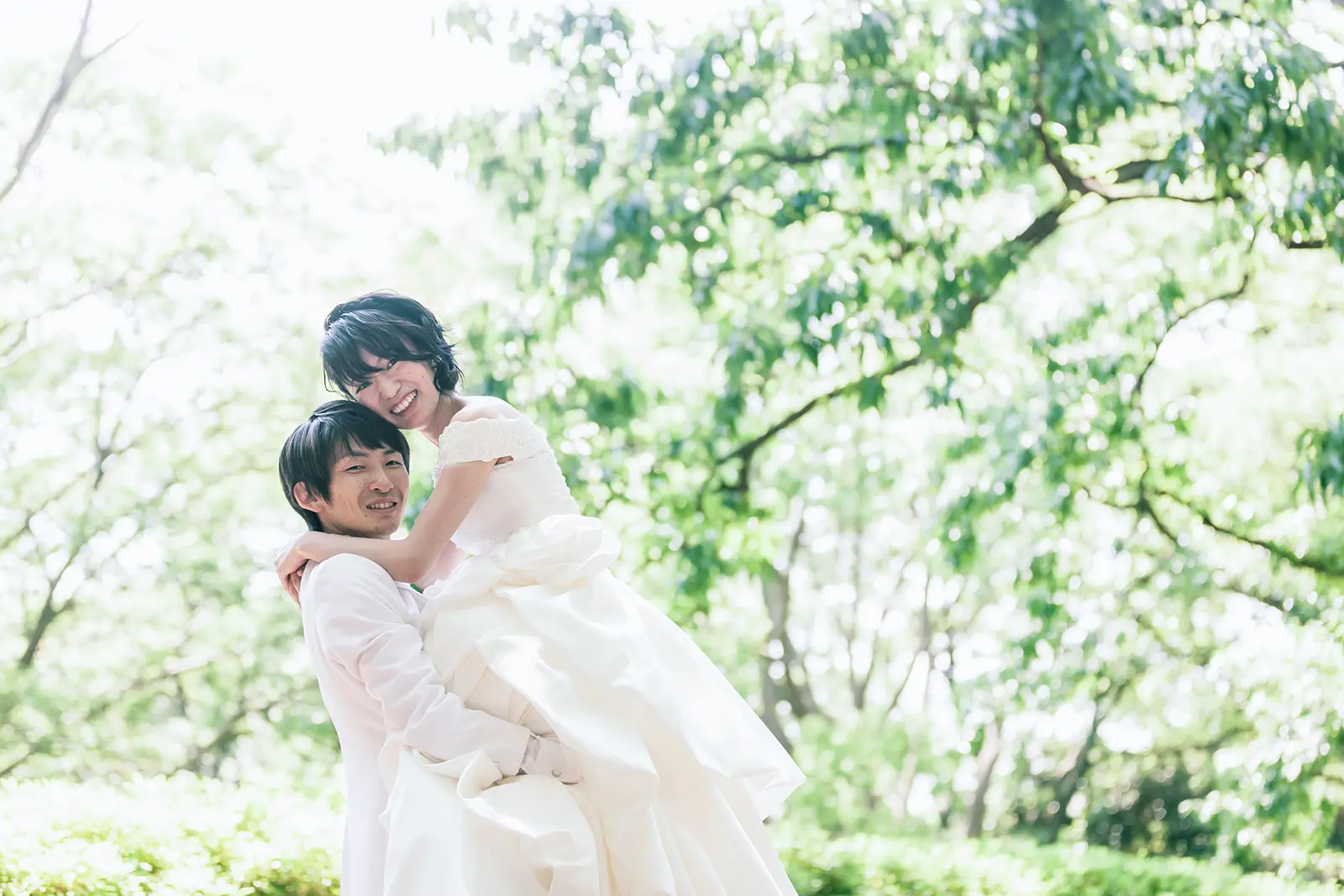 緑の中で新郎が新婦を抱き上げて笑うフォトウェディング写真