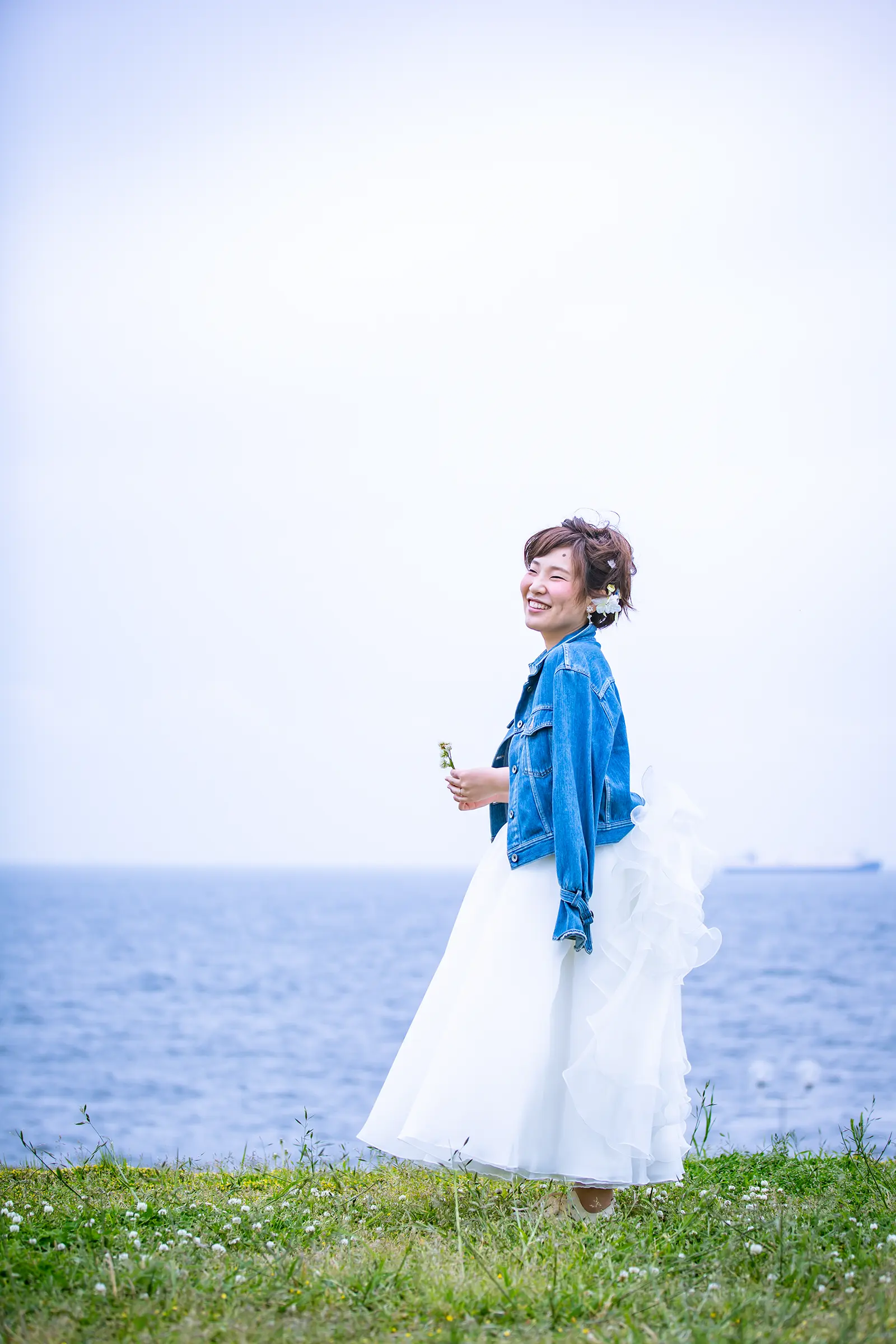 デニムジャケットを羽織って海辺に立つ新婦を写したフォトウェディング写真