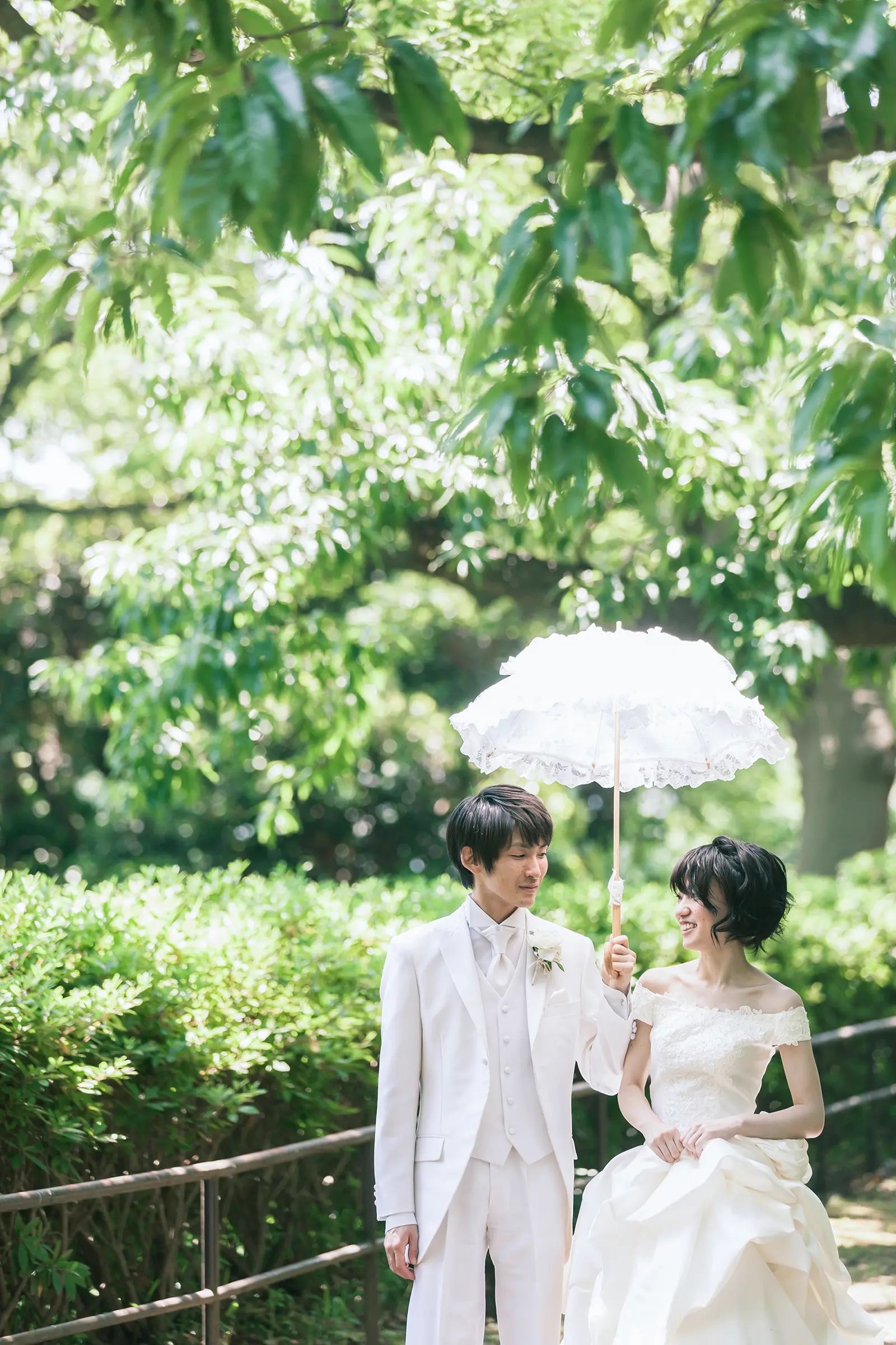 レースの日傘を持って並ぶ新郎新婦を写したガーデンフォトウェディング写真
