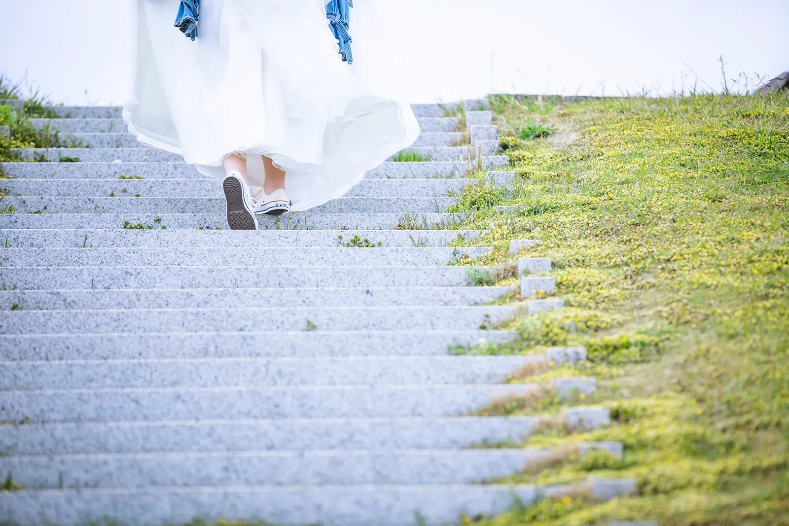 ドレス姿でスニーカーを履き階段を上がる新婦の足元を写した写真