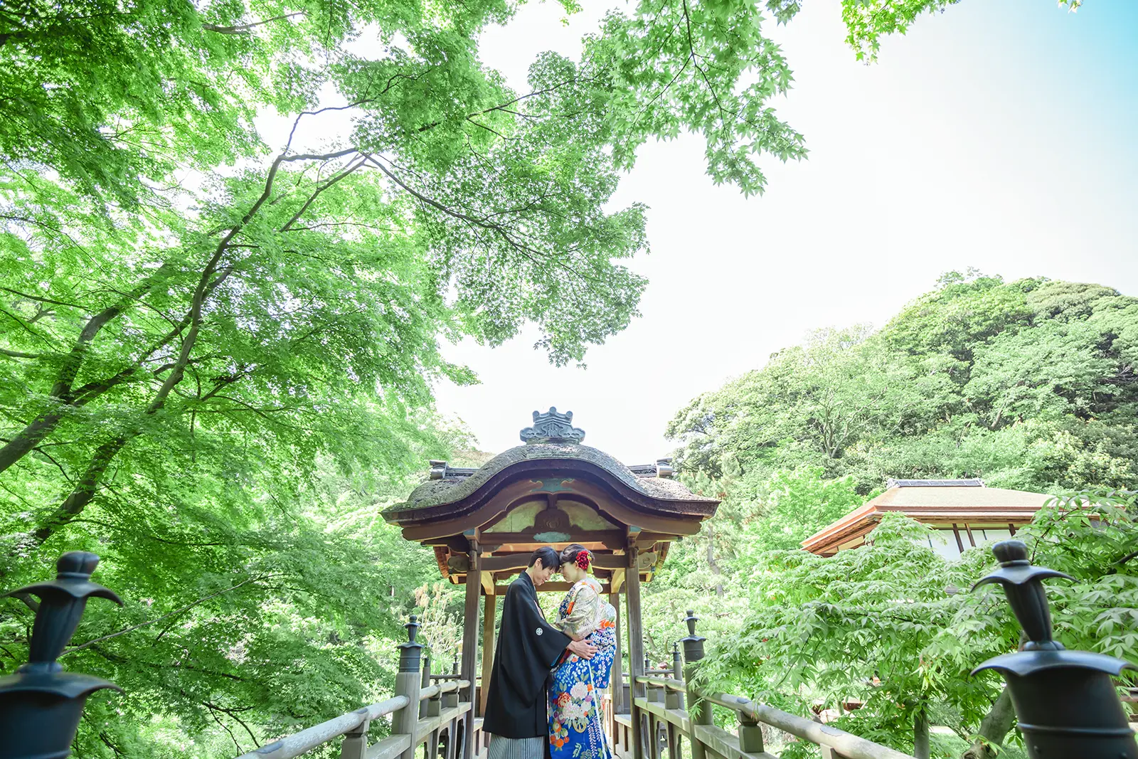 横浜の三溪園で新緑に囲まれた橋の上で寄り添う和装姿の新郎新婦