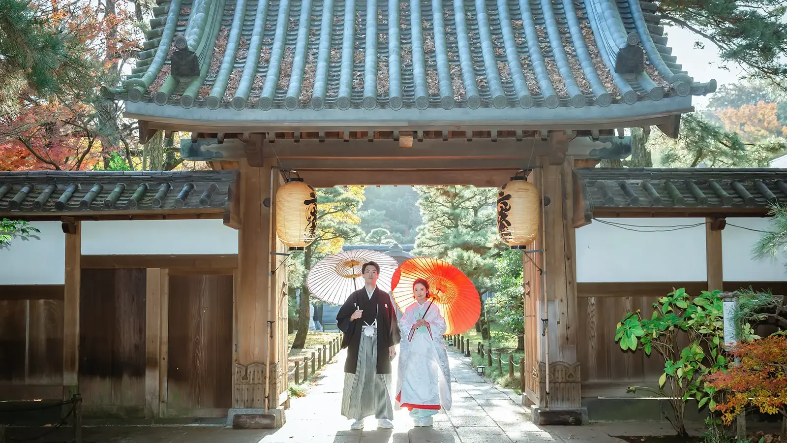 横浜の三溪園の門前で和傘を持って並ぶ和装姿の新郎新婦
