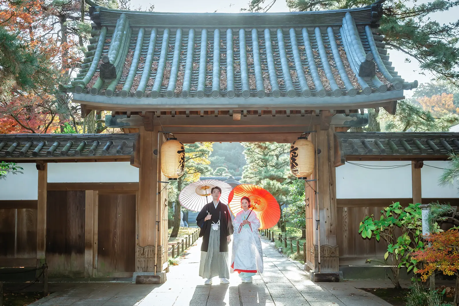 横浜の三溪園の門前で和傘を持って並ぶ和装姿の新郎新婦