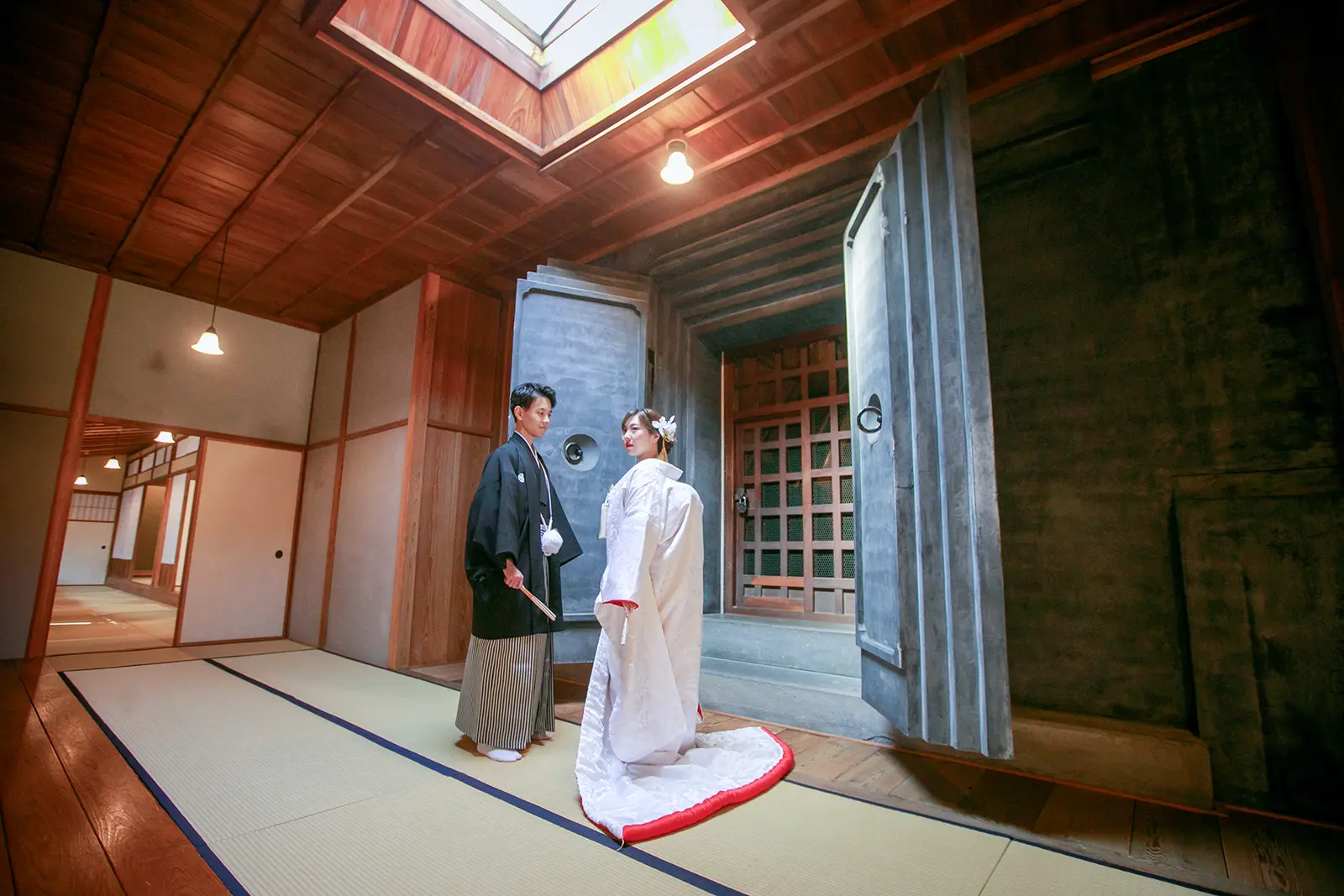 横浜の三溪園で蔵のある屋内空間に立つ白無垢姿の新婦と紋付袴の新郎