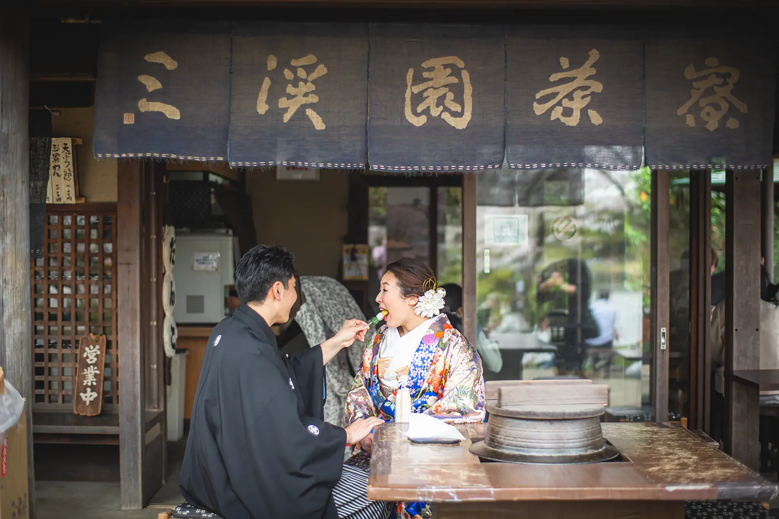 横浜の三溪園の茶店で和装姿の新郎新婦が食べ歩きを楽しむ様子