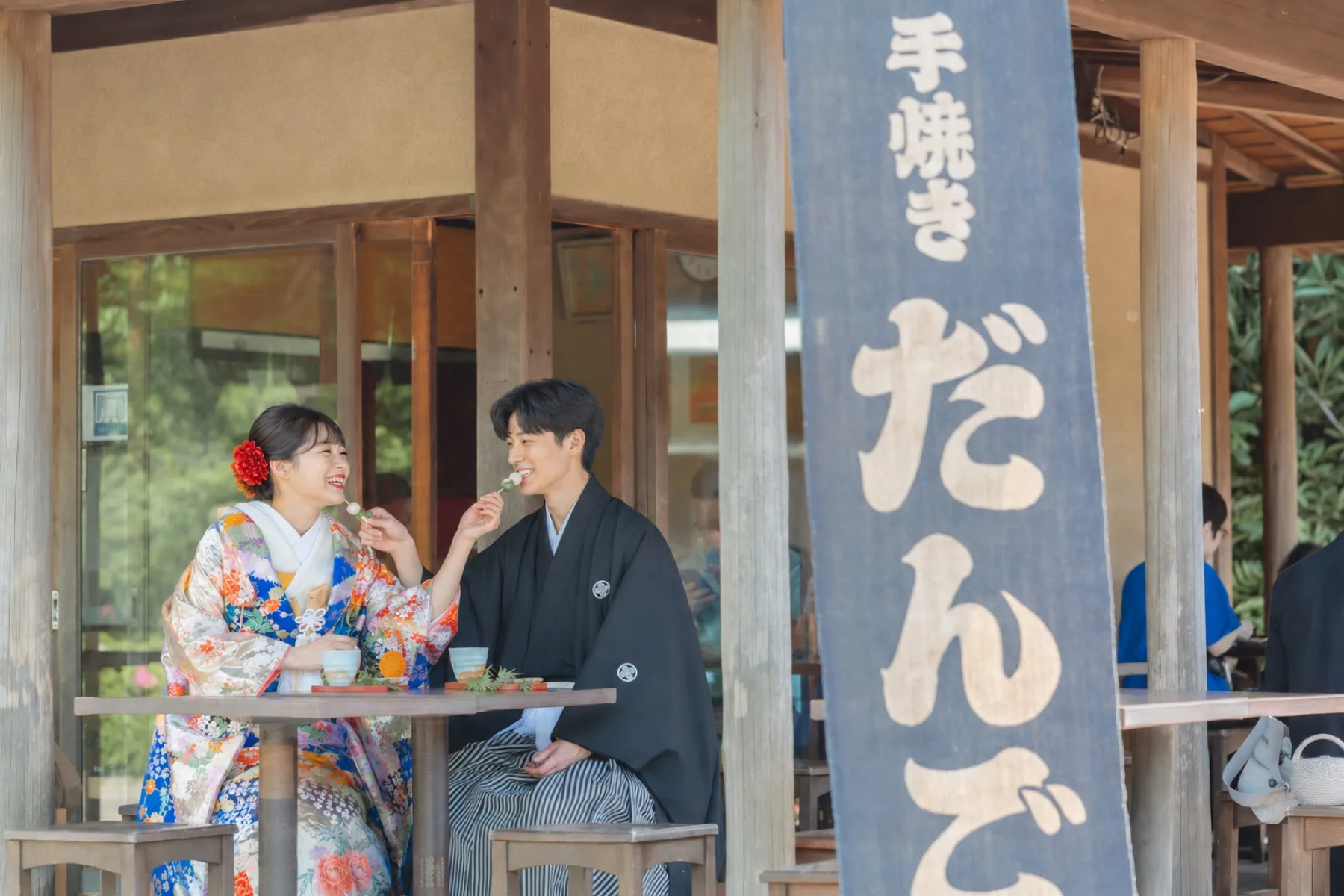 三溪園の茶屋で団子を手に笑い合う色打掛の新婦と紋付袴の新郎、横浜の和装ロケーション撮影
