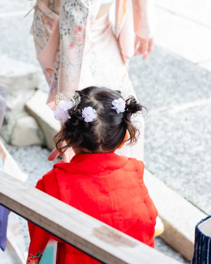 くせ毛の3歳の女の子を後ろから。両サイドに小さなお団子を作り、白い小花の飾りをつけている