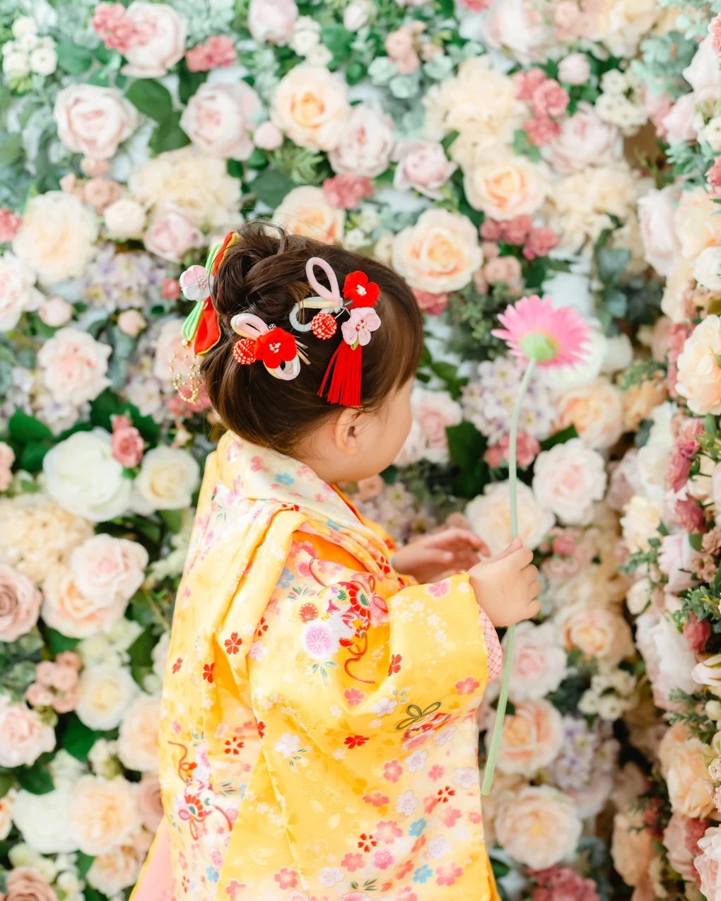 ハーフアップに小さなお団子を作り、赤いつまみ細工の飾りを散らした3歳の女の子の後ろ姿