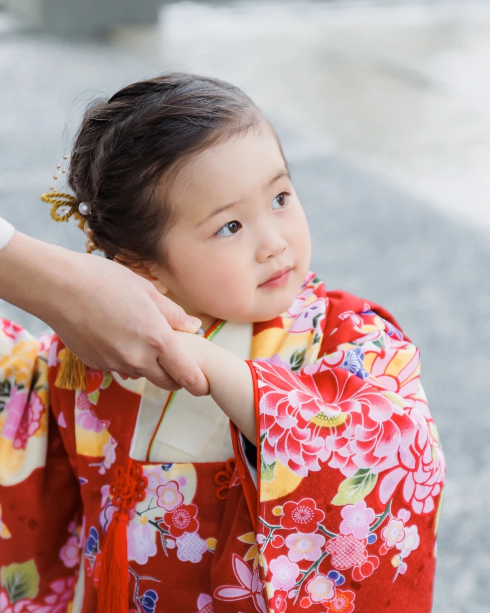 髪をすっきりまとめて金色の髪飾りをつけた3歳の女の子の横顔。赤い花柄の着物姿
