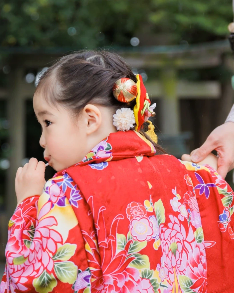 大きなリボンと白い花の髪飾りをつけた3歳の女の子の横顔。赤い花柄の着物姿