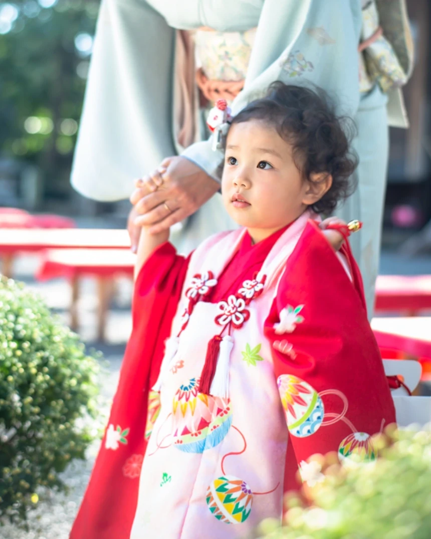 短いくせ毛の3歳の女の子が母親と手をつなぐ。髪は結ばずにおろし、小さな髪飾りを添えている