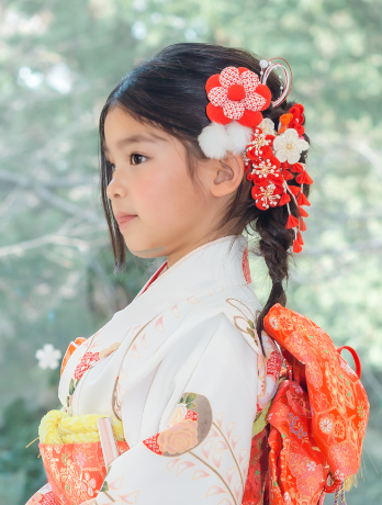 七五三で7歳の女の子の髪型のアップ。ロングの髪を編みおろしに、赤い花飾り