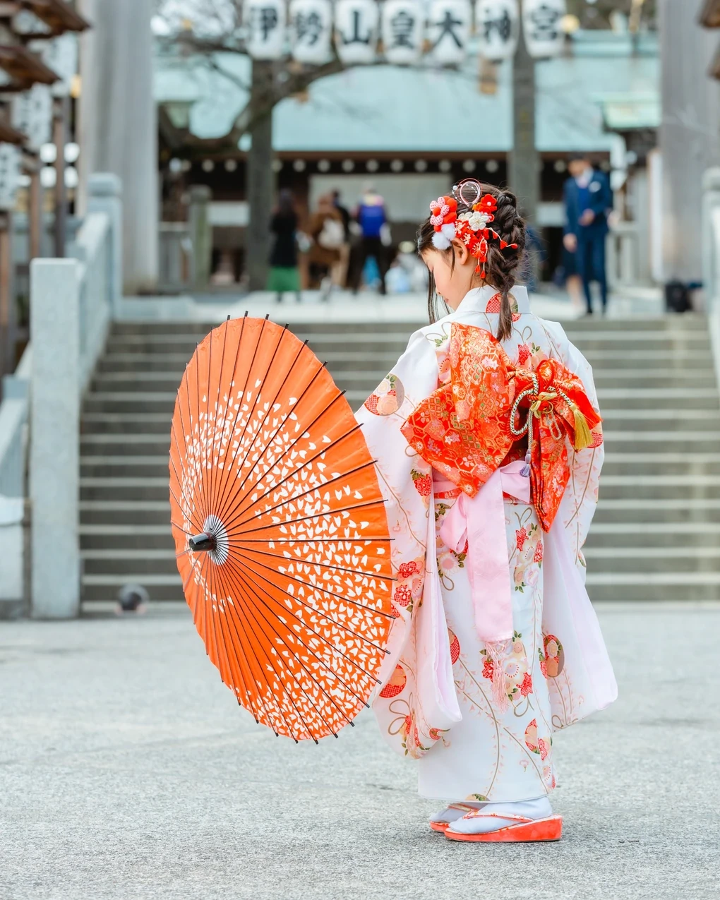 神社の石段の前で、和傘を持つ七五三7歳の後ろ姿。白い着物に編みおろし