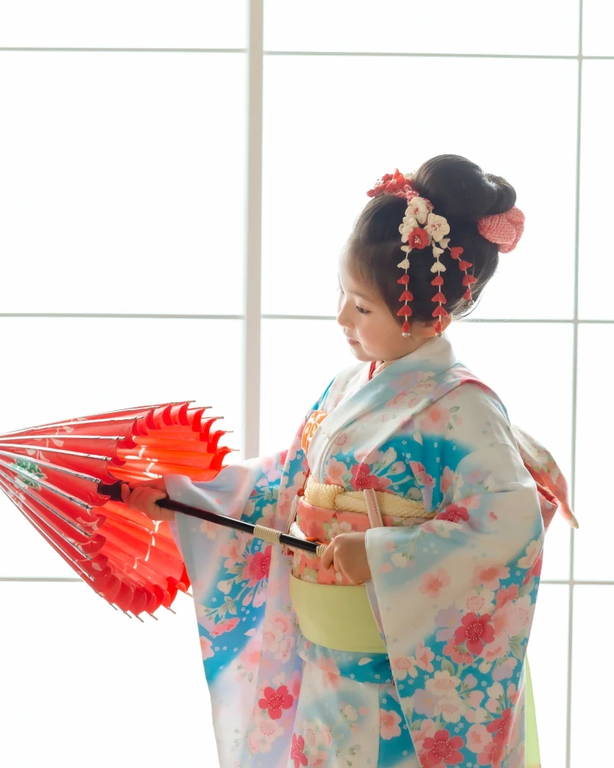 和傘を持つ七五三7歳の女の子の横顔。日本髪風アップにピンクの鹿の子と赤白の下がり飾り