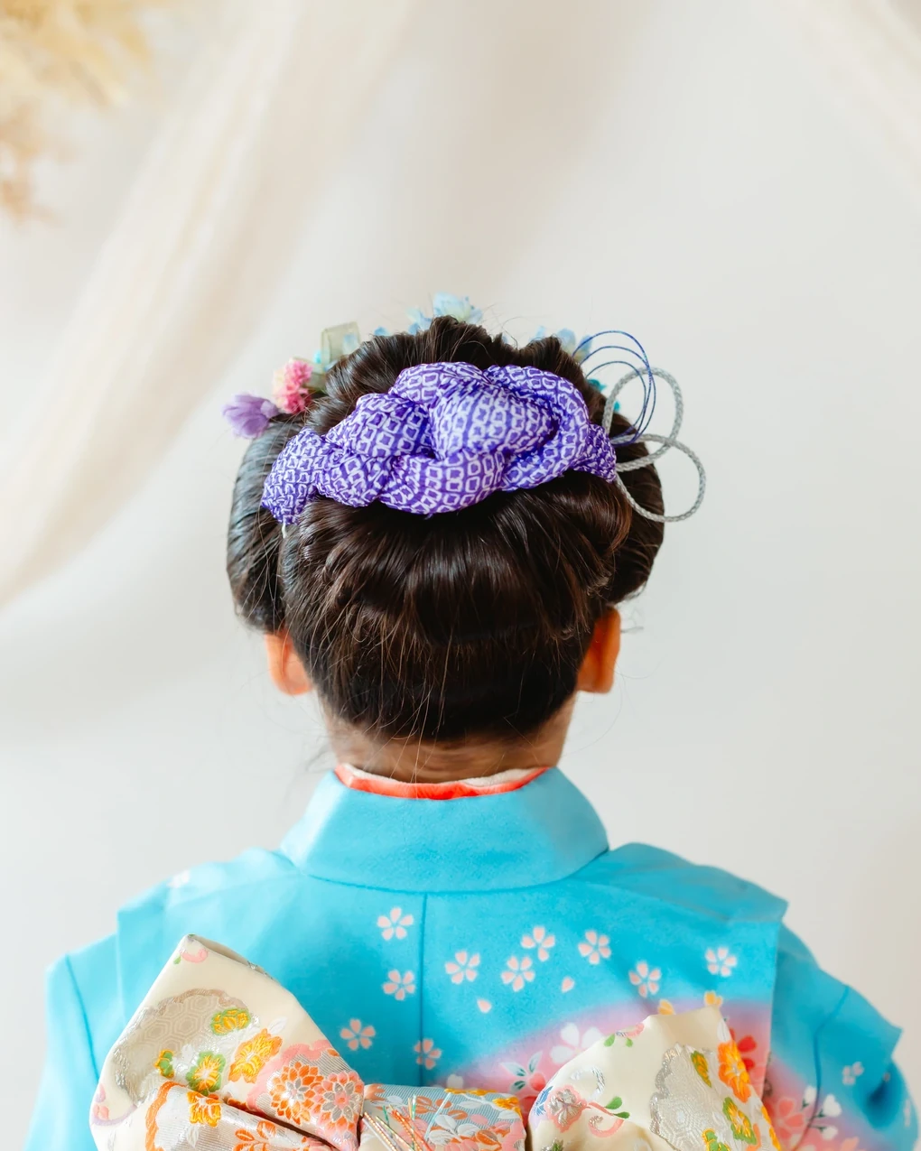 七五三7歳の日本髪風の後ろ頭。水色の着物に紫の鹿の子と水色の花、銀のループ飾り