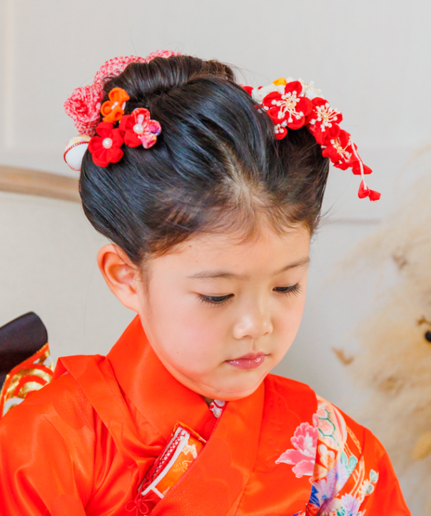 七五三で7歳の女の子の髪型のアップ。前髪なしの日本髪風に、両サイドの赤いつまみ細工