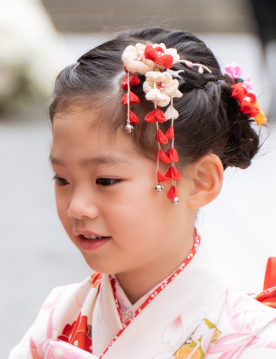 七五三で7歳の女の子の髪型のアップ。前髪なしの編み込みアップに赤い飾りと下がり飾り