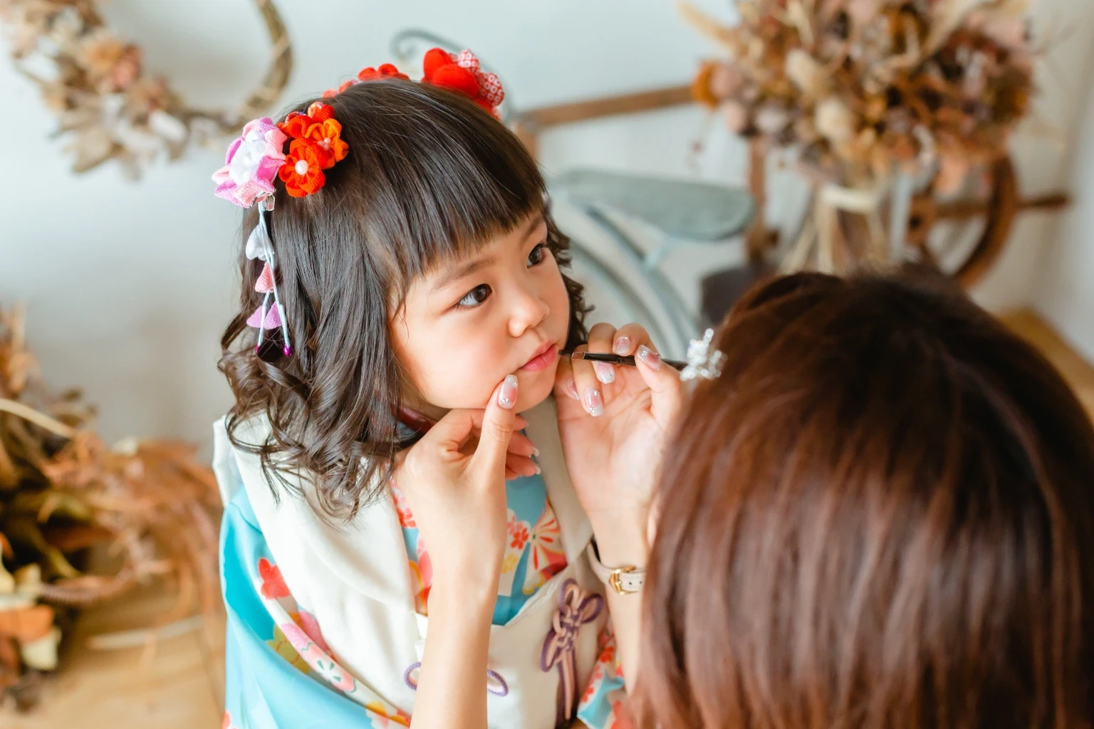 花の髪飾りをつけたくせ毛のボブの女の子が、スタッフに口もとを整えてもらっているお支度の様子