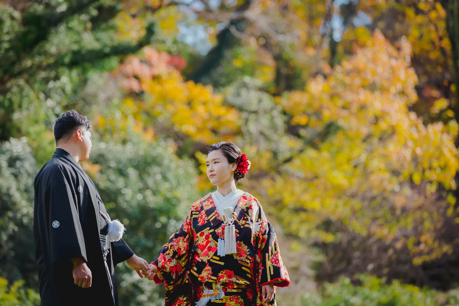 称名寺の黄色く色づいた木々の間を、黒地に花柄の色打掛の新婦と紋付袴の新郎が手をつないで歩く