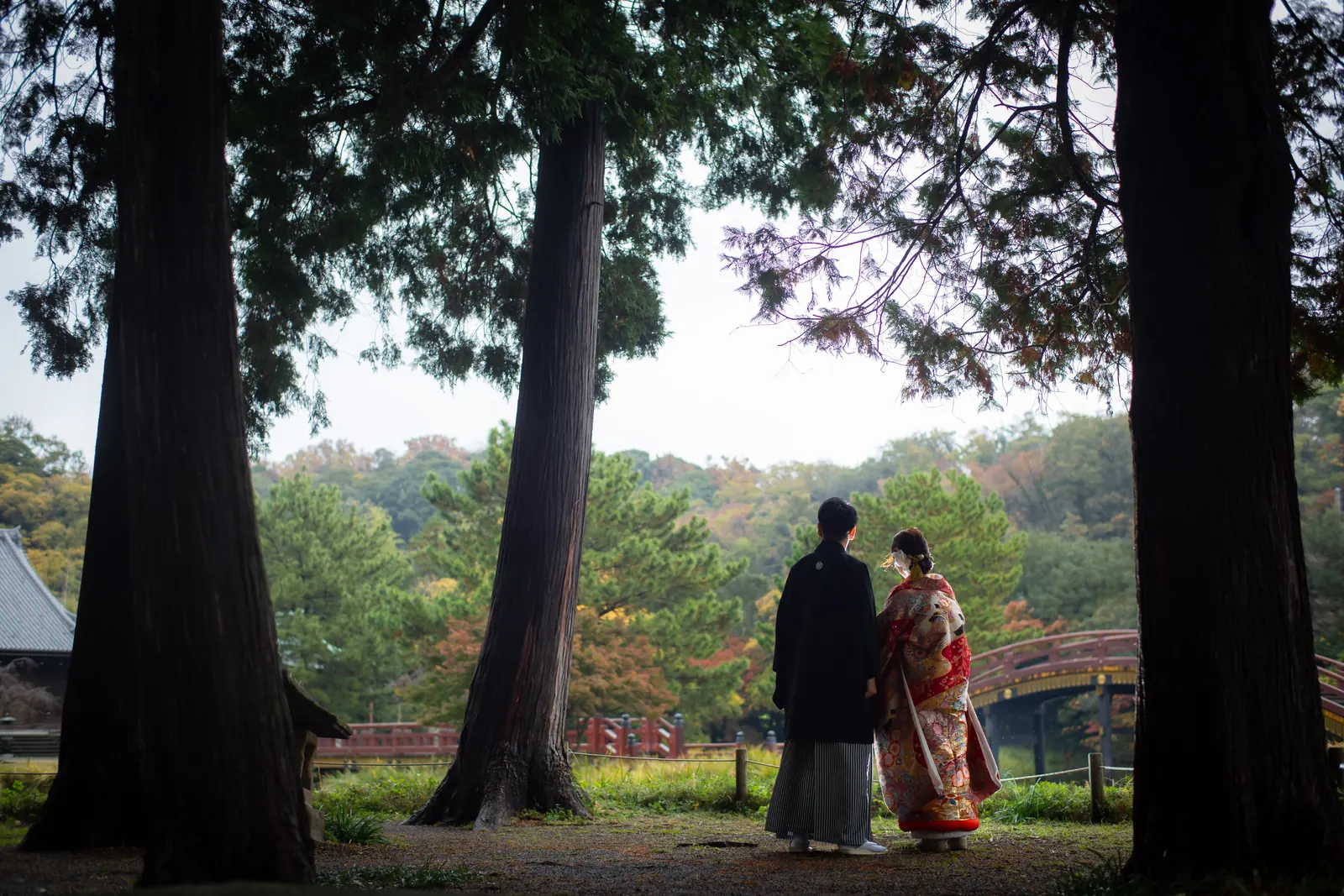 称名寺の大きな木立の間から、参道に立つ色打掛の花嫁と紋付袴の新郎を写した引きの一枚