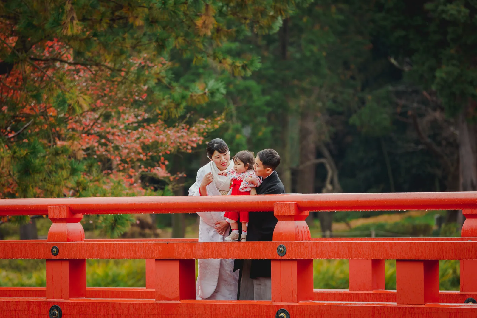 称名寺の朱塗りの反橋の上で、白無垢の新婦と紋付袴の新郎が、赤い着物のお子さまをはさんで寄り添っている