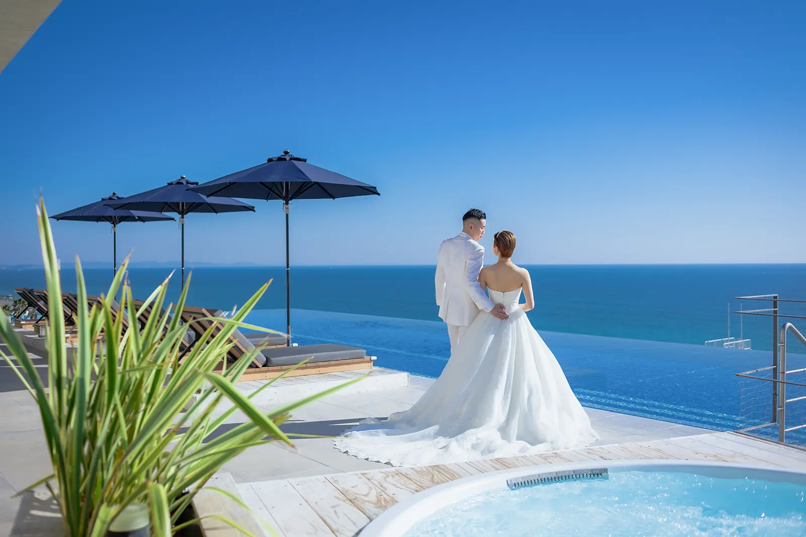 大磯プリンスホテルを背景に青い海と空に包まれて立つ新郎新婦のフォトウェディング