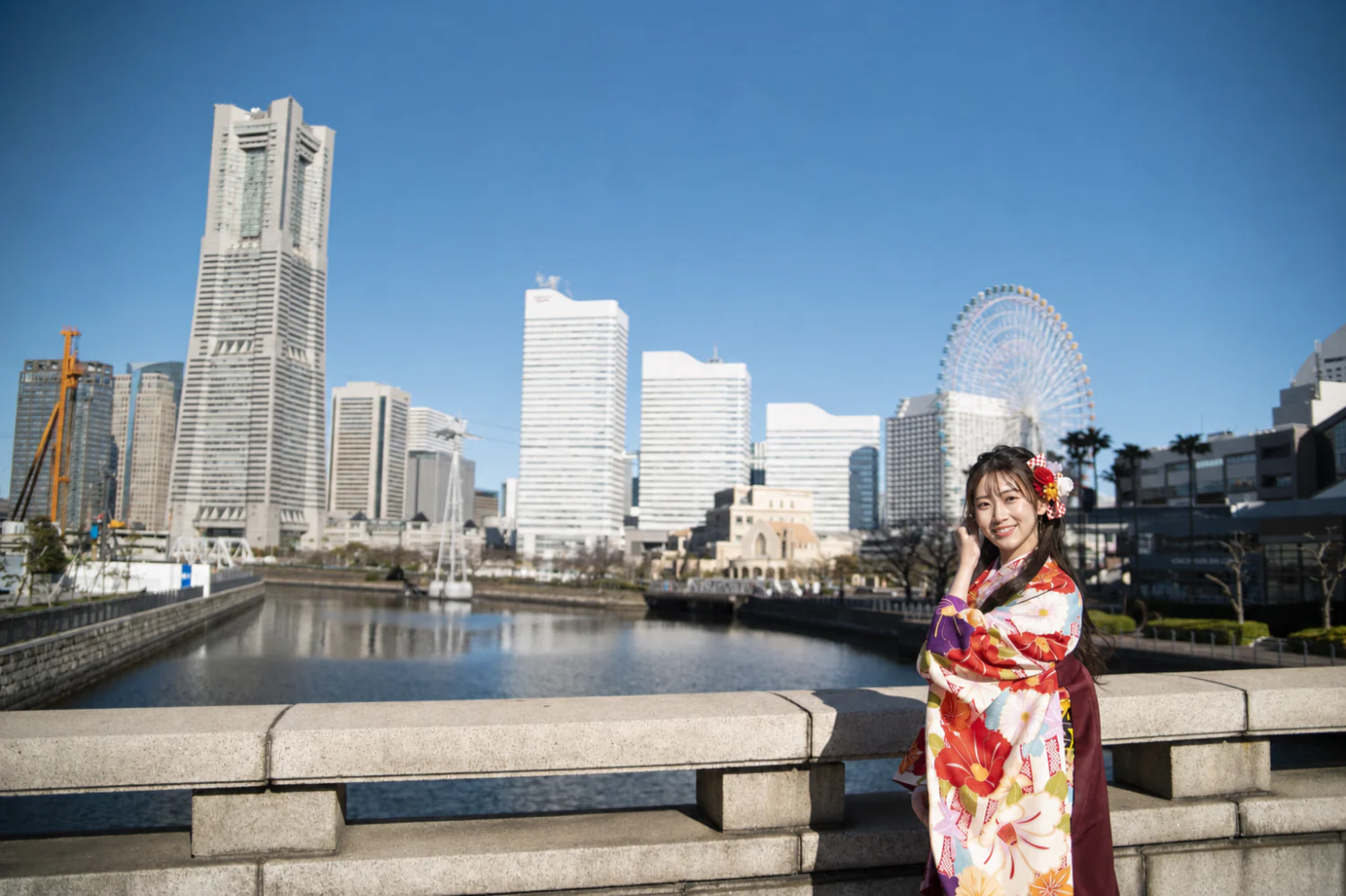 横浜みなとみらいの水辺で卒業袴を着た女性の前撮り写真。ランドマークタワーと観覧車を背景にした横位置カット