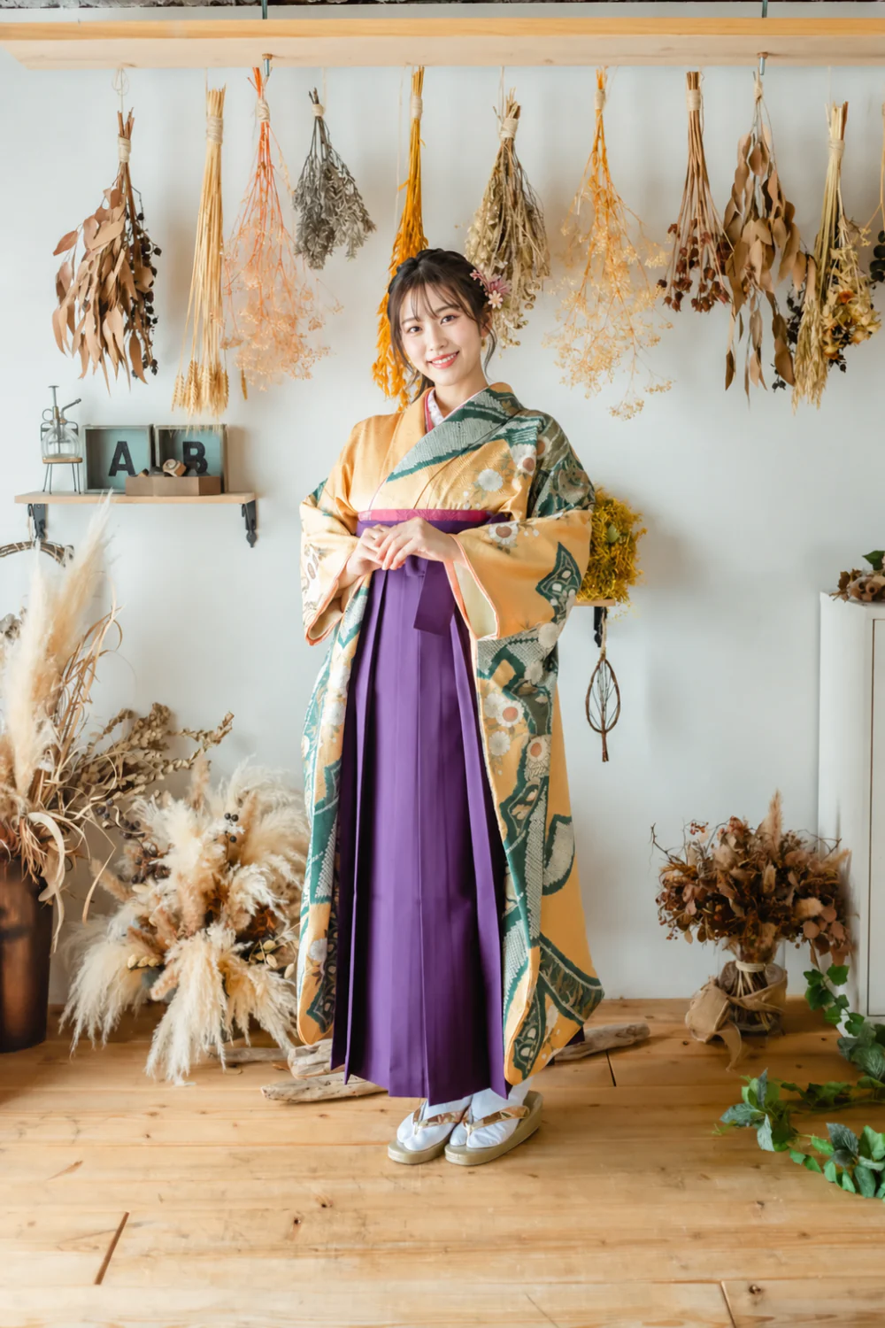 ドライフラワーで装飾したスタジオで、紫の袴とクリーム地の古典柄着物を着た女性の全身前撮り写真