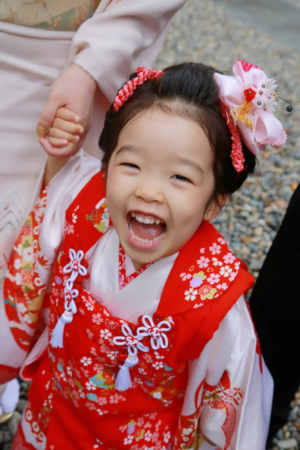 母と手をつなぎ口を大きく開けて笑う3歳の女の子、赤い被布姿の七五三を俯瞰で撮影（相州春日神社・横浜）